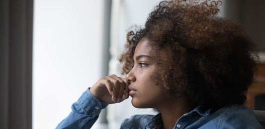 Close up side profile view face of African sad thoughtful teenager girl sit on sofa at home looking into distance feels unhappy, first unrequited love, teen relation problem, break up, worries concept