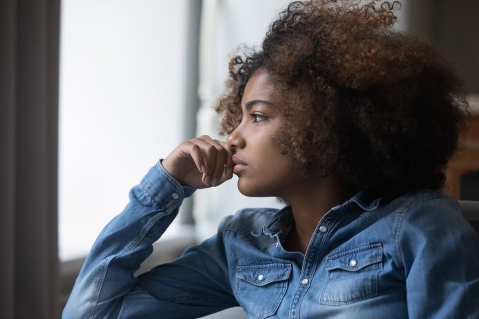 Close up side profile view face of African sad thoughtful teenager girl sit on sofa at home looking into distance feels unhappy, first unrequited love, teen relation problem, break up, worries concept