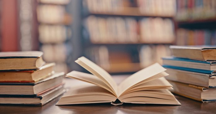 Library, books on table and background for studying, learning and research in education, school or college. Reading, philosophy and open, vintage or history print book, university blurred background