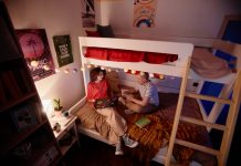 High angle view at two young students doing homework together sitting on bunk bed and in college dorm, copy space