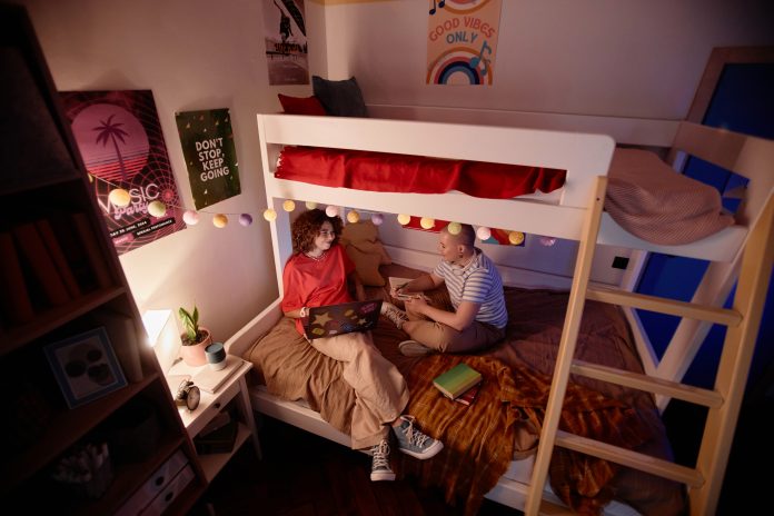 High angle view at two young students doing homework together sitting on bunk bed and in college dorm, copy space