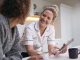 Mature Woman In Dressing Gown At Home Talking With Female Nurse With Digital Tablet