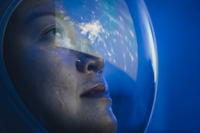 Asian chinese mid adult female astronaut looking at earth through window from spaceship at outer space