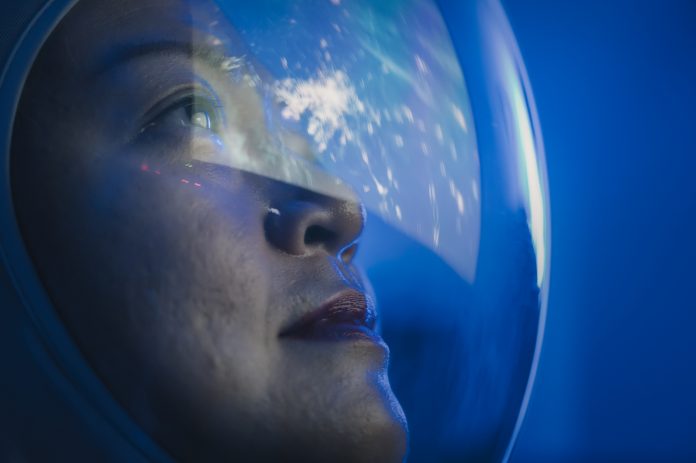 Asian chinese mid adult female astronaut looking at earth through window from spaceship at outer space