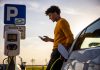 African american man using mobile phone while he is waiting for his electric car to be charged at charging station