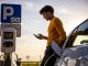 African american man using mobile phone while he is waiting for his electric car to be charged at charging station