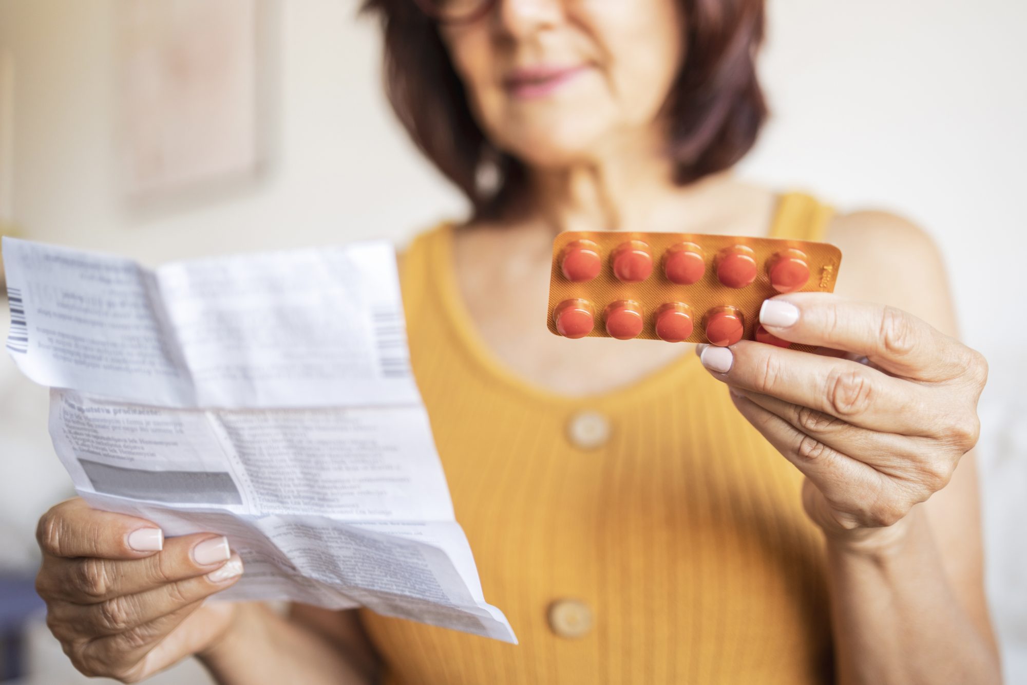 Close up of a Latin woman using medicine pills. She is sitting on bed and reading patient information leaflet.