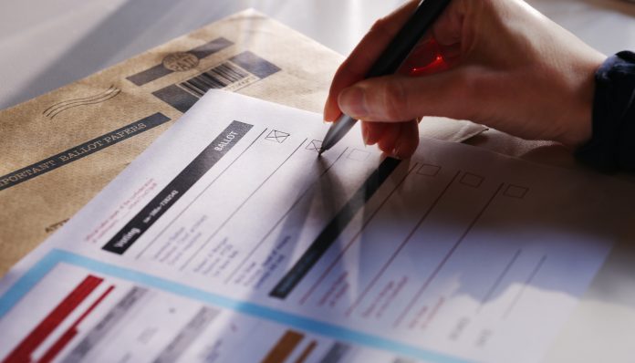 Stock image showing a woman’s hand filling in a postal ballot / voting form.