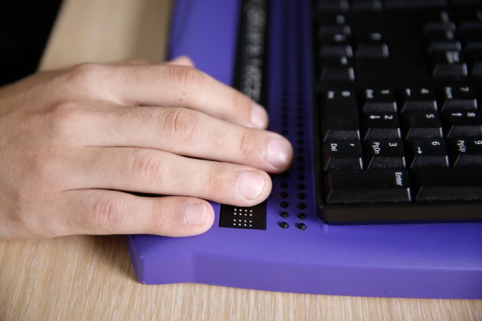 Blind person using computer with braille computer display and a computer keyboard. Blindness aid, visual impairment, independent life concept.