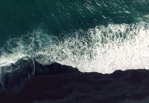 Cold ocean waves washing down the black sand beach making a lot of ocean foam. The video is taken by drone which goes down to 350 meters and rotates.