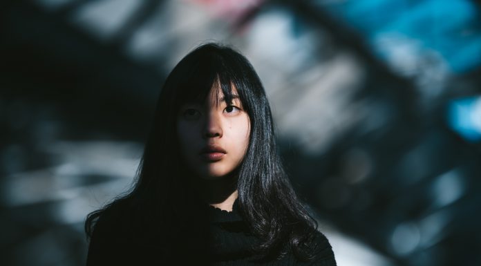 A portrait of a young Asian woman while half of her face is lit by the sun and the other half is in the shadow.