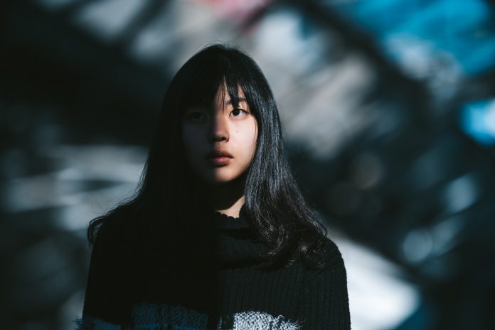 A portrait of a young Asian woman while half of her face is lit by the sun and the other half is in the shadow.