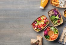 Healthy take away food and drink in disposable eco friendly paper containers on gray wooden background, top view. Fresh salad, soup, poke bowl, vegetable, fruits, chicken wrap and juice.