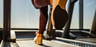 Close up of unrecognizable athletic woman exercising on treadmill in a health club. Copy space.