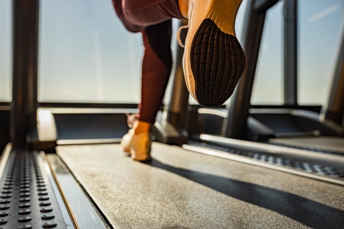 Close up of unrecognizable athletic woman exercising on treadmill in a health club. Copy space.