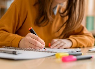 Young unrecognisable female college student in class, taking notes and using highlighter. Focused student in classroom. Authentic Education concept.