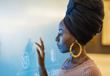 A young African-American woman in her 20s wearing a turban and large earrings, touching a giant interactive display screen.