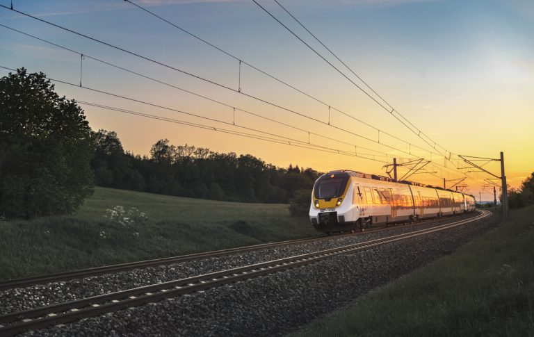 Modern regional train traveling with speed on railway tracks through nature landscape, at sunset, near Schwabisch Hall, Germany.