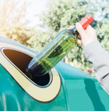 Hand throwing glass bottle in recycling bin