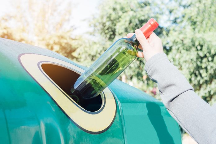 Hand throwing glass bottle in recycling bin