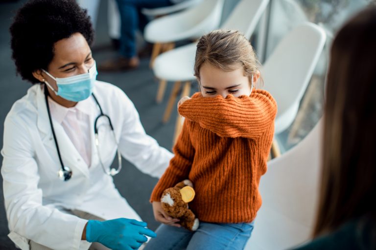 liittle girl coughing with doctor sat next to her