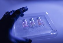 Close-up hand of medical worker with surgical gloves holding a set of deep frozen COVID-19 (SARS-CoV-2) coronavirus vaccine vials. Blue abstract background.