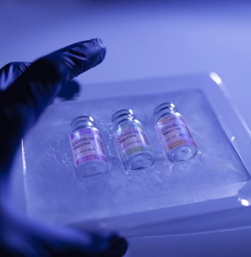 Close-up hand of medical worker with surgical gloves holding a set of deep frozen COVID-19 (SARS-CoV-2) coronavirus vaccine vials. Blue abstract background.