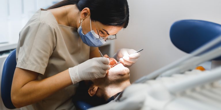 Group portrait of two people, woman dentist making treatment in modern clinic for man. Medical concept photography indoors for dentistry. Dental office, doctor working in clinic with patient.