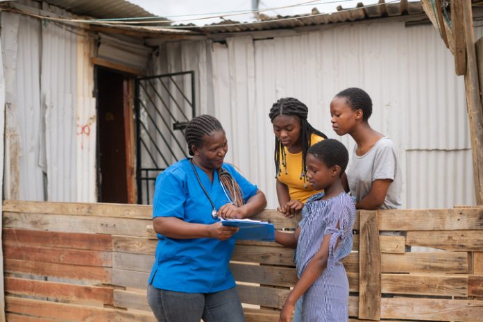 Community Nurse talking to teenage girls in an informal settlement infront of a shack