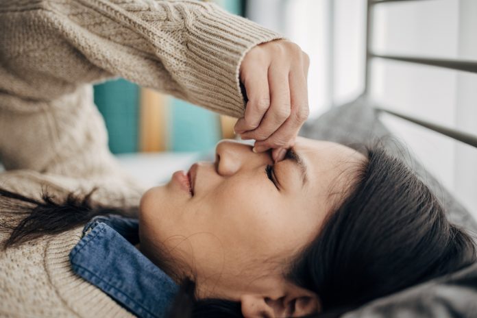 One woman, Japanese woman having headache while lying on bed in her bedroom at home.