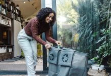 Young multiracial woman sorting plastic waste in recycling bags in front of the house