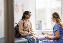 The young adult female patient smiles while listening to the nurse give an encouraging update regarding her medical exam that was recently completed.