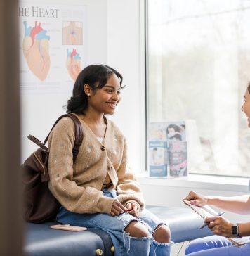 The young adult female patient smiles while listening to the nurse give an encouraging update regarding her medical exam that was recently completed.