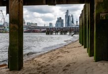A view from under the pier of the Thames Beach on the south bank of the River Thames with a view of the skyscrapers in the City of London.