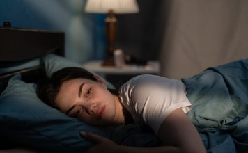 Young sad woman lying in bed late at night trying to sleep suffering insomnia. Girl in bed scared on nightmares looking worried and stressed. Sleeping disorder and insomnia concept