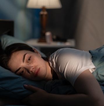 Young sad woman lying in bed late at night trying to sleep suffering insomnia. Girl in bed scared on nightmares looking worried and stressed. Sleeping disorder and insomnia concept