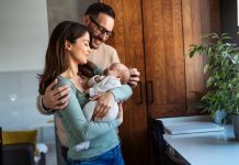 Portrait of young happy man and woman holding newborn cute babe dressed in white unisex clothing.