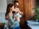 Portrait of young happy man and woman holding newborn cute babe dressed in white unisex clothing.
