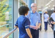 a business woman chats to a doctor and senior staff nurse in a busy hospital corridor