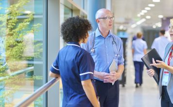 a business woman chats to a doctor and senior staff nurse in a busy hospital corridor