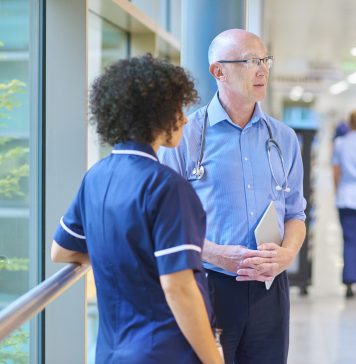 a business woman chats to a doctor and senior staff nurse in a busy hospital corridor