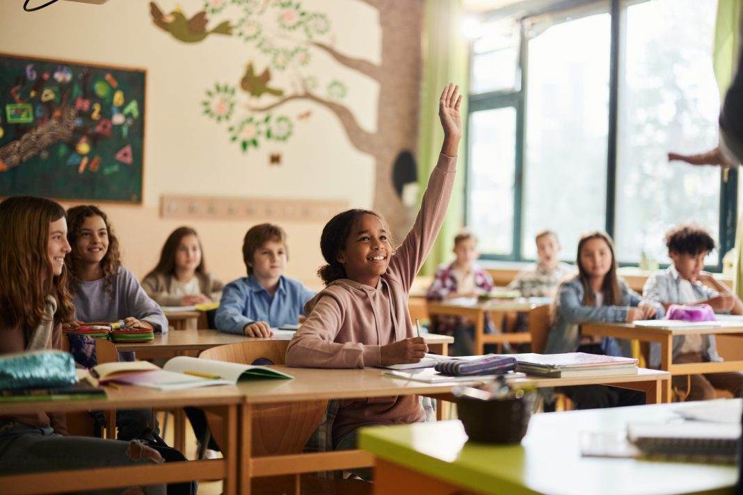 African American schoolgirl raising her hand to answer the question on a class in the classroom.