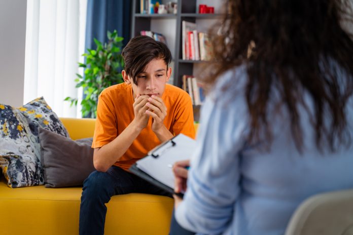 Female psychologist counseling teenage boy in office, Young people's mental health