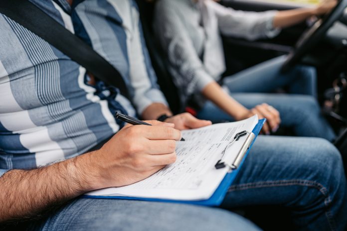 Young Driving Instructor Grading His Female Student Using A Checklist