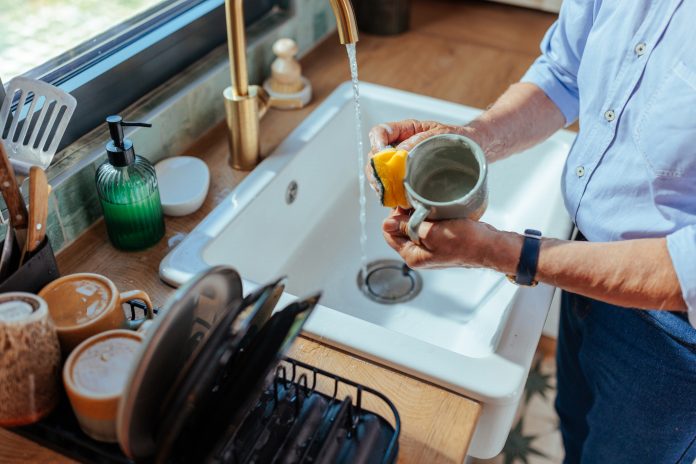 A senior man washing a mug with a kitchen sponge