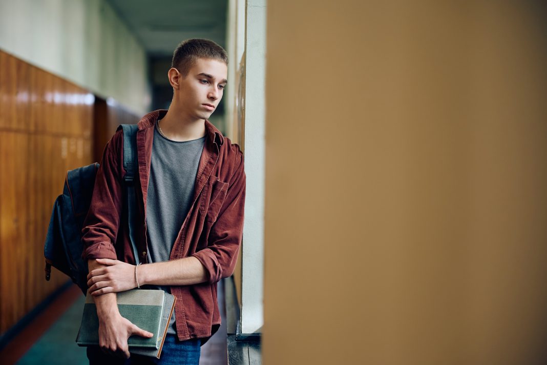 Sad teenage boy thinking of something while standing in hallway at high school. Copy space. article covering: Right-wing ethno-nationalists and jihadi Salafists