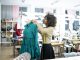 Skilled experienced worker or fashion designer in a professional atelier smiling while standing in front of a mannequin with a tape measure on her neck.
