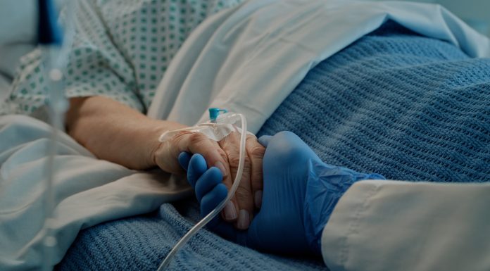 Hospital, holding hands and bed with doctor, support and care together in a clinic after surgery. Senior, healthcare and cancer patient with empathy, kindness and caregiver with compassion with help