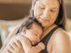 An adorable photo of a three (3) month old baby girl sleeping on her mother's chest. Her mother is looking down at her baby daughter with a soft smile on her face.