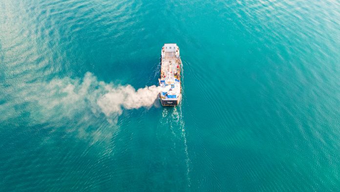 Aerial view of a container ship carrying cargo for an import-export logistics business in the ocean. Smoke from a ship sailing in the ocean